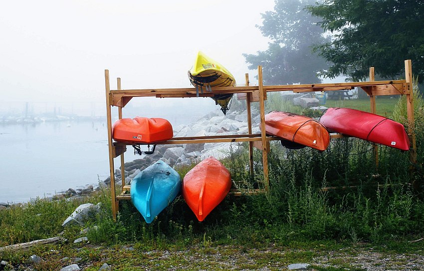 Six kayaks of various colors are stored on a DIY wooden rack