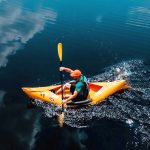 A man paddles a yellow folding kayak in the open waters