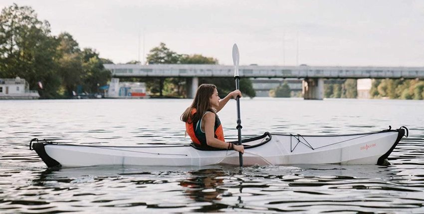 A girl paddles a white folding kayak