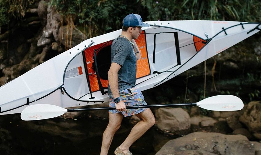 A man carries a white folding kayak