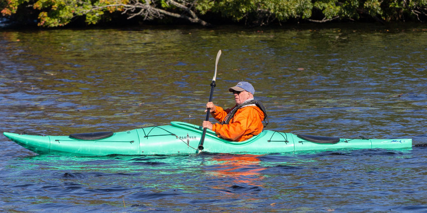 A man paddles a green folding kayak