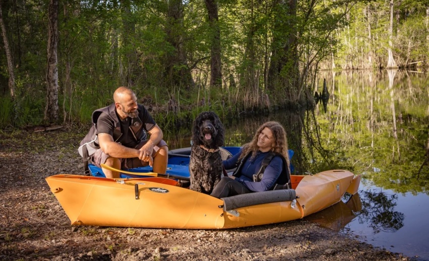 A family and their dog sit in plastic folding kayaks on the forest lake shoe