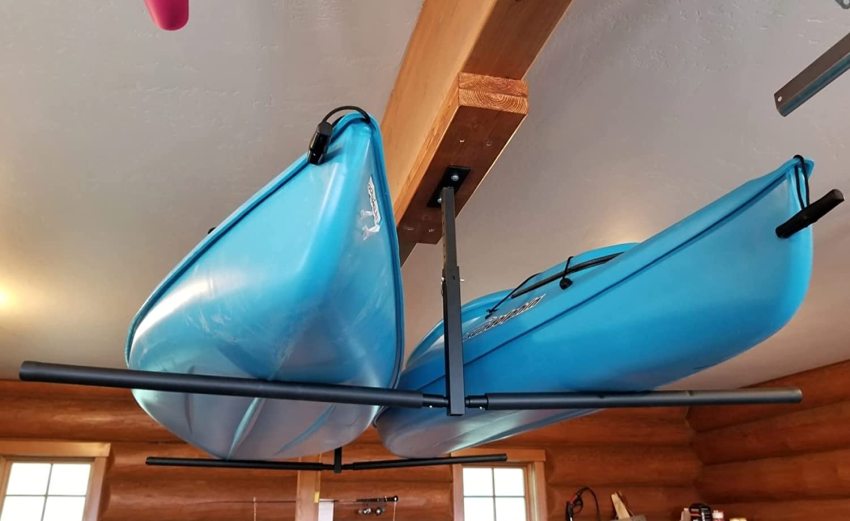 Two blue plastic kayaks are stored on ceiling racks in a garage