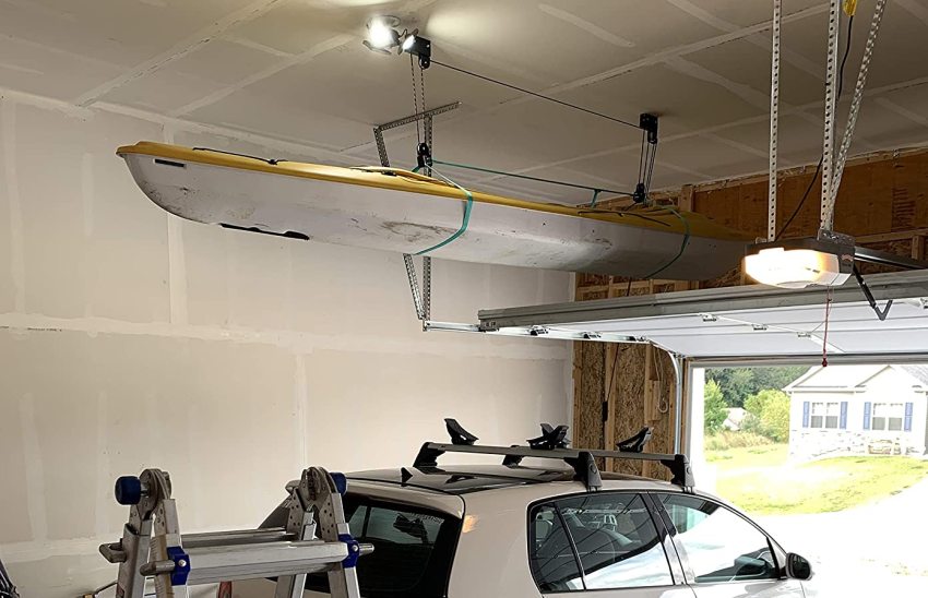 A yellow-white plastic kayak hangs on a hoist above a vehicle in a garage
