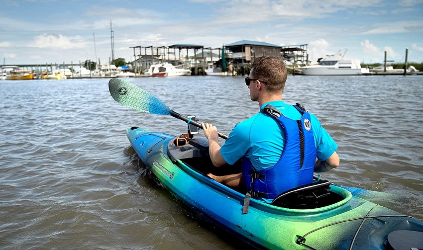A man in a blue PFD paddles his recreational kayak on a lake