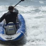 A man paddles his white and blue inflatable kayak in whitewater