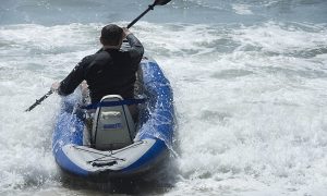 A man paddles his white and blue inflatable kayak in whitewater