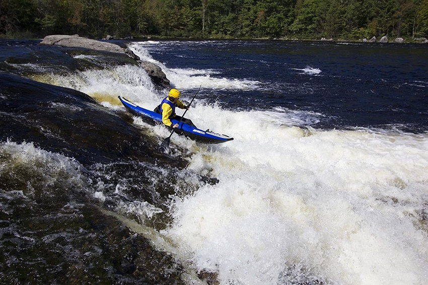 A man in a yellow helmet and blue PFD paddles his white and blue kayak in the whitewater