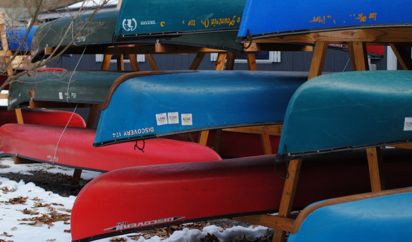 Multiple canoes of different colors are stored on racks
