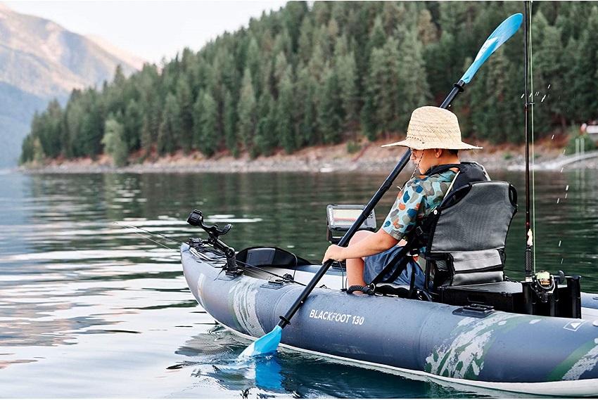 A boy paddles his inflatable fishing kayak on a lake