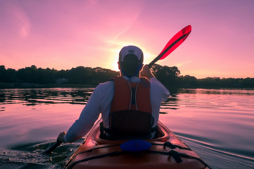 A man in a red PFD paddles his kayak on a lake