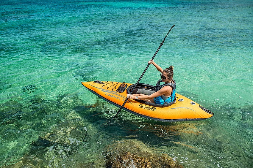A girl in a blue PFD paddles her yellow inflatable kayak in coastal waters