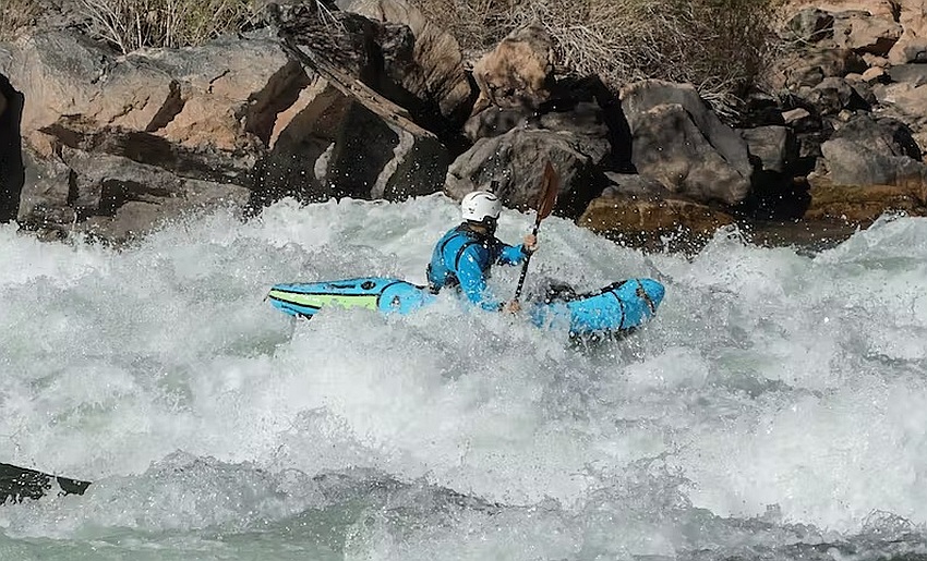 A man paddles a blue inflatable kayak in the whitewater