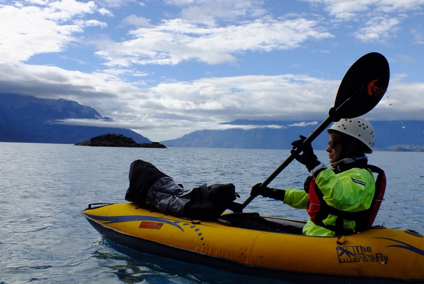 A woman in a green jacket and a red PFD paddles a yellow Advanced Elements Firefly kayak on open water