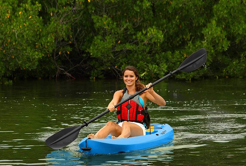 A woman in a red PFD paddles a blue sit-on kayak on a river
