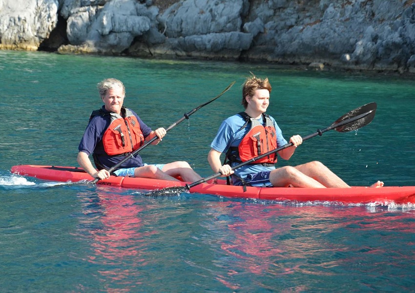 A boy and a man in red PFDs paddle a red modular kayak