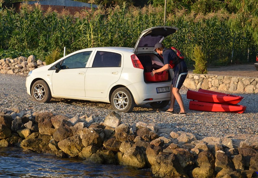 A man unloads components of a red modular kayak from a white car