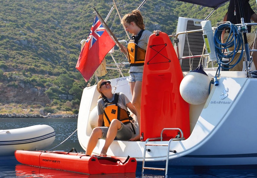 A girl and a woman are on a yacht's stern, assembling components of a red modular kayak