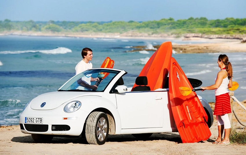 A man and a woman with paddles in their hands stand near a white car and red components of a red modular kayak