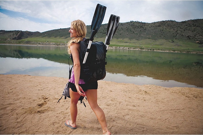 A woman carries the Sevylor Quikpak K1 kayak and a paddle packed in a bag on her back
