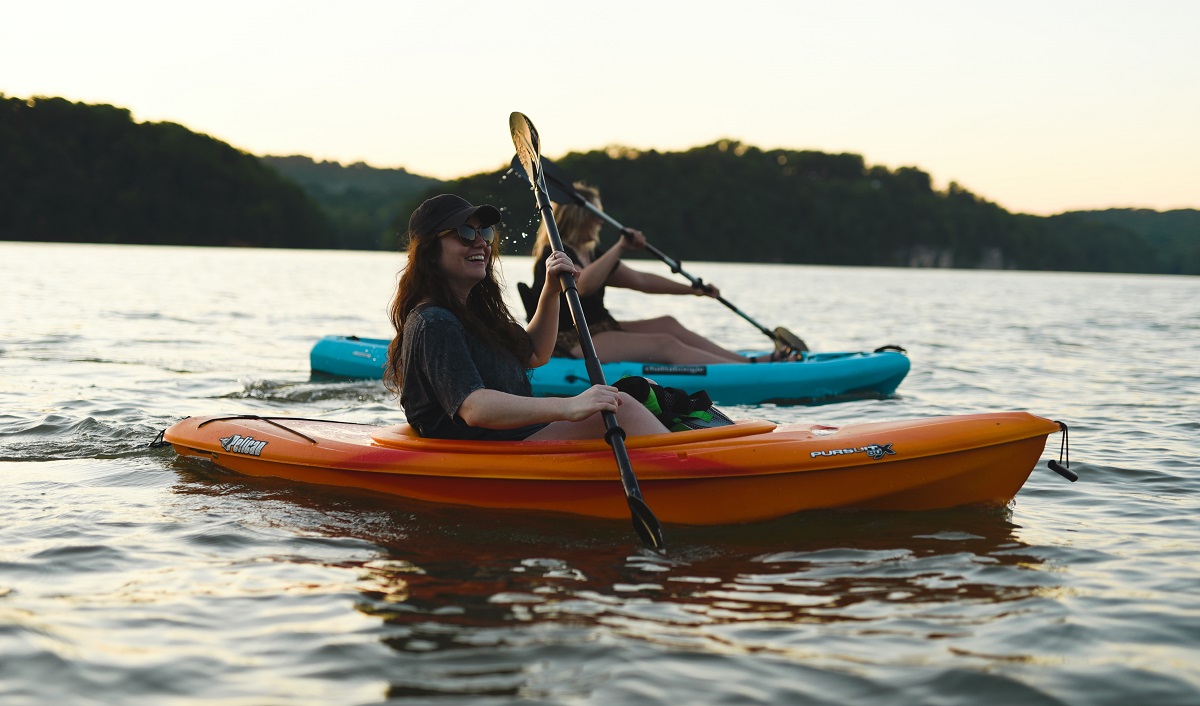 Two women paddles a blue and an orange sit-in kayaks on open water