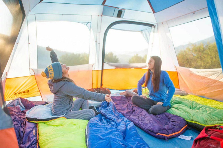 Two women sit inside the Eureka Copper Canyon LX 12 Person Tent with open mesh windows
