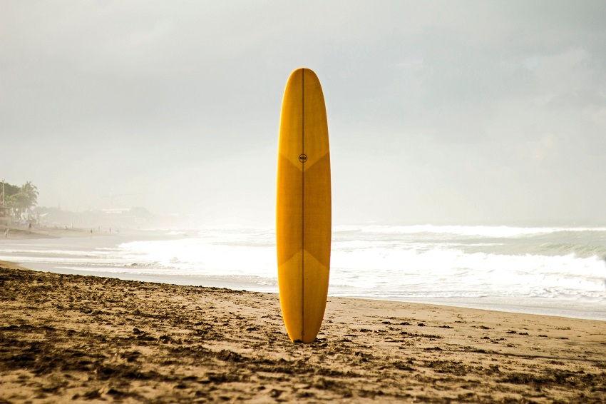 A wooden paddle board stands vertical on the beach