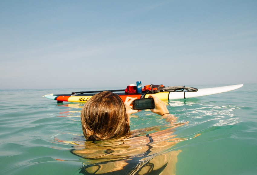 A woman takes a photo of her SUP with gear from the water