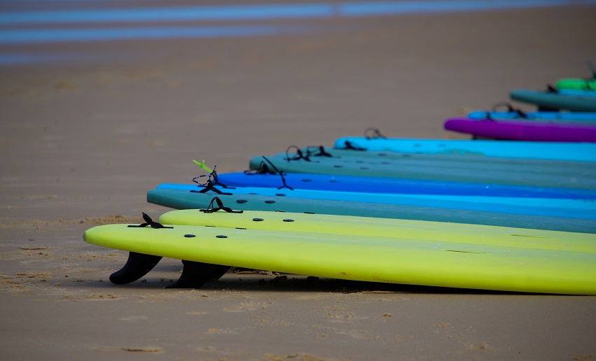 Plastic paddle boards of different colors lie on the beach