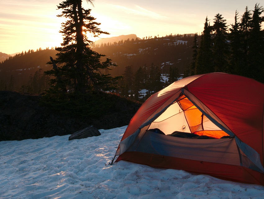 A tent with open door is set up on snow in a forest