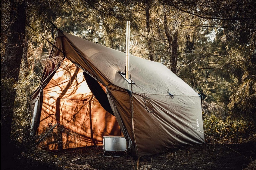A green tent with a camping stove inside is pitched in a forest