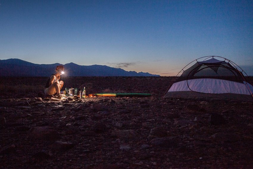 A woman with a headlight on her head is cooking near a camping tent