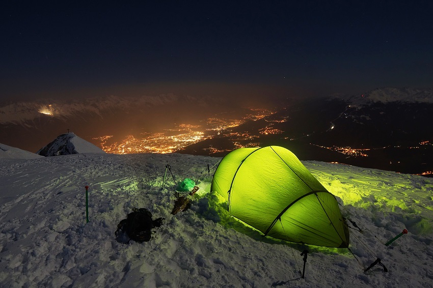 A green illuminated tent, pitched on a snowy slope at night