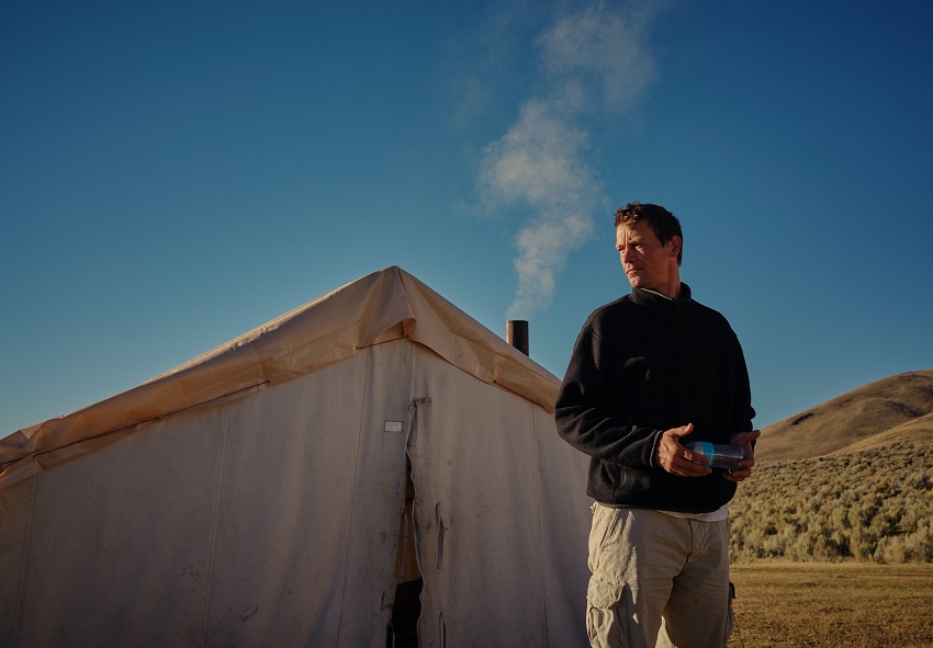 A man with a plastic bottle in his hands stands in front of a white canvas tent with a stove jack