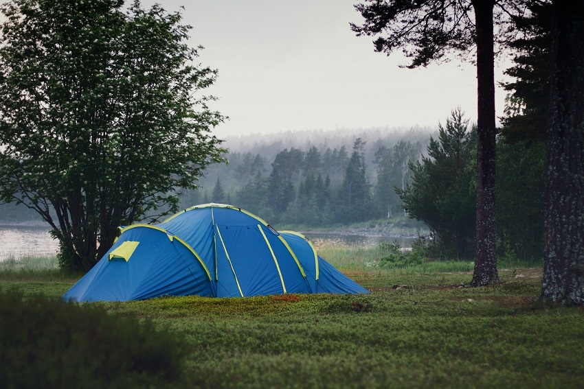 A blue tent is pitched near a lake on a rainy day