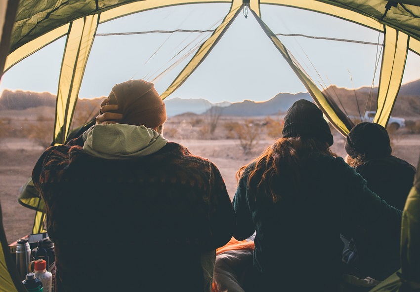 Three people sit inside a camping tent with open mesh walls