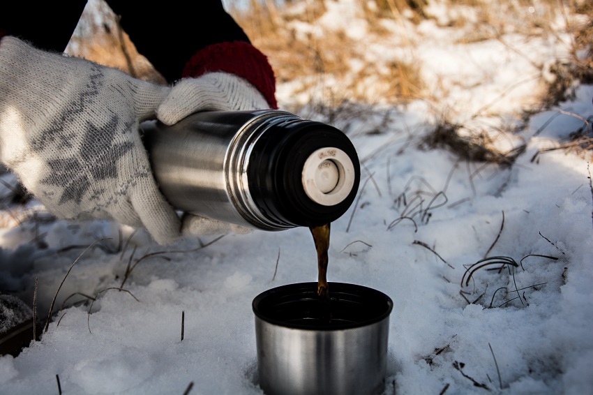 Human hands pour coffee from a thermos into its cup  