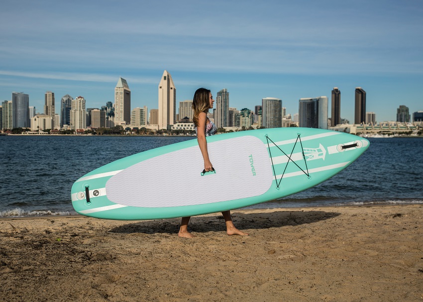 A woman carries a green and white SUP at the city waterway