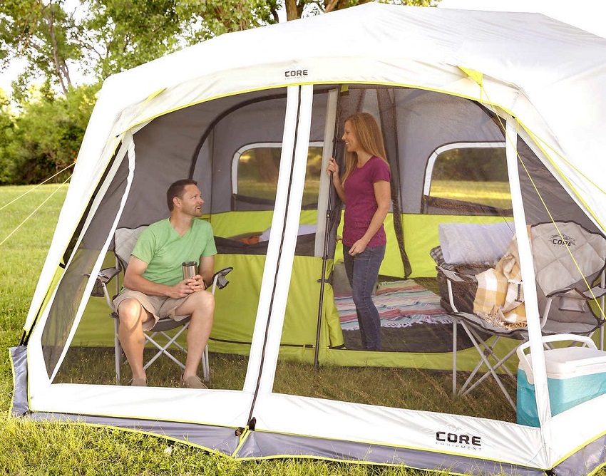 A man sits in a chair inside a tent's screen room and talks to a woman standing in the open door inside the CORE 10-Person Instant Cabin Tent