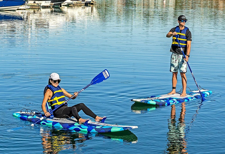 A man stands on a blue foam paddle board, while a woman paddles a blue paddle board sitting on it