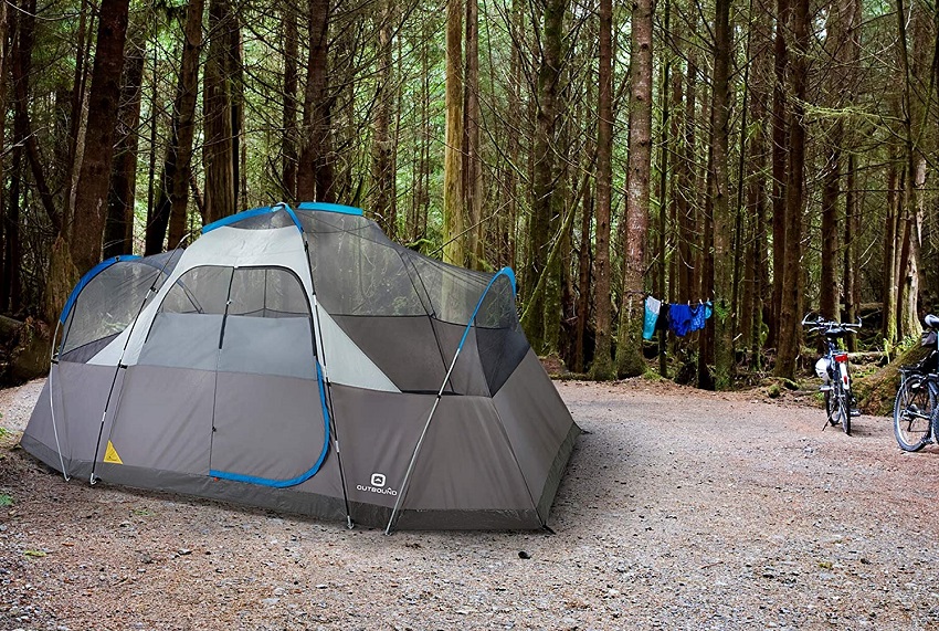 A 12-person camping tent is pitched in the woods. 2 bicycles are parked nearby.