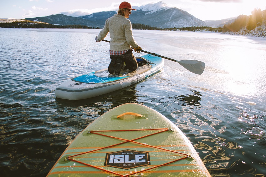 A woman with a paddle sits on an inflatable paddle board on a lake