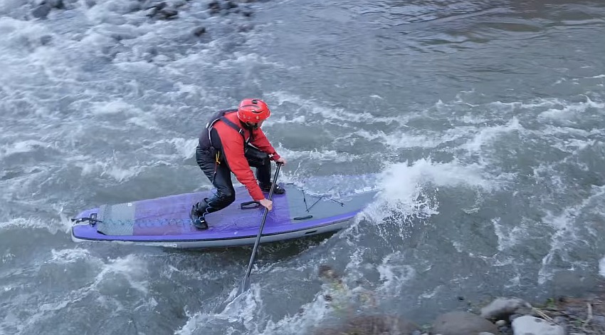 A man in a red helmet paddles his SUP in whitewater