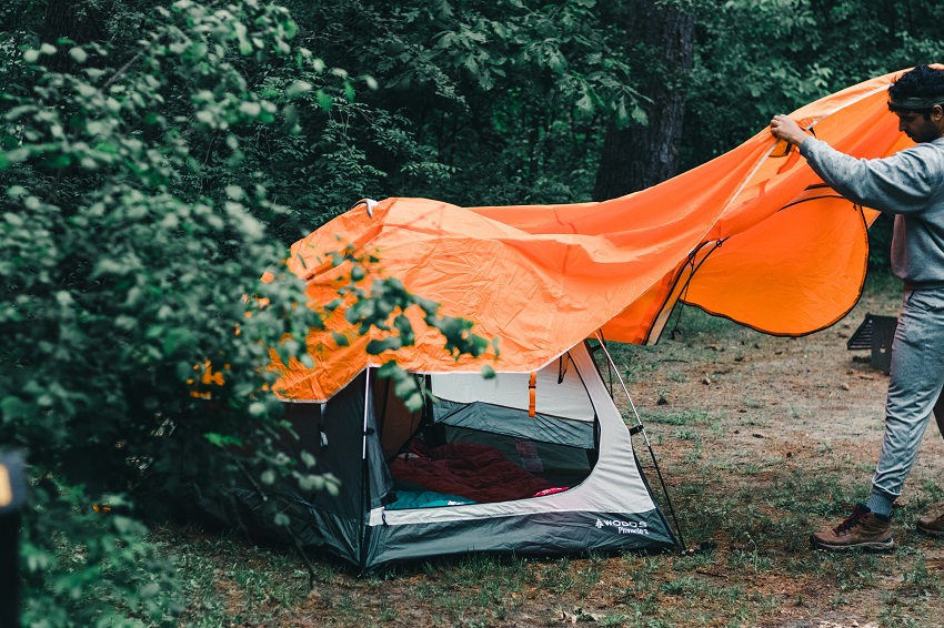A man covers a camping tent with a orange rainfly