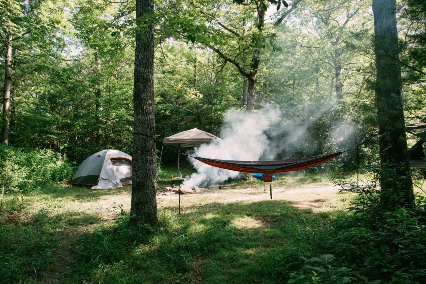 A campsite with a tent, a canopy and a hammock in the forest