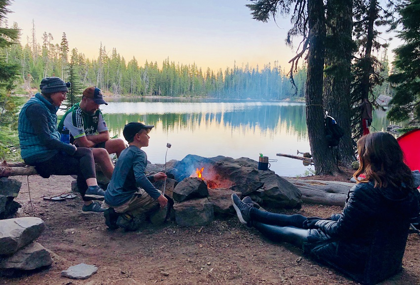 A family sits around a campfire near a lake