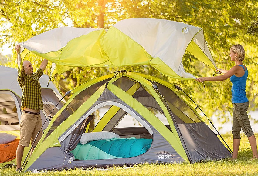 A man and a woman are covering the Core Equipment 4-Person Instant Dome Tent with a rainfly