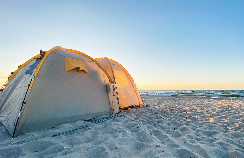 A white camping tent is pitched on the sandy shore