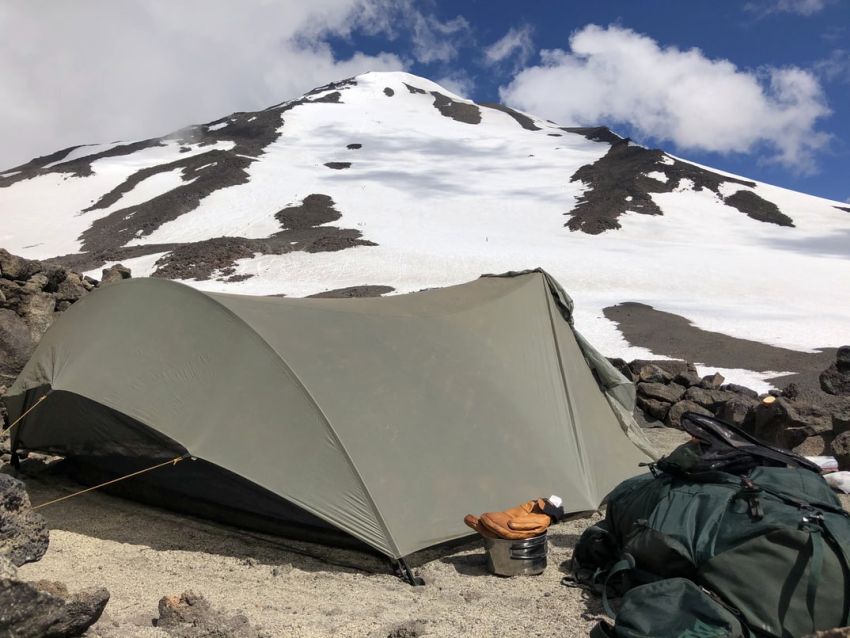A green tent is pitched on a snowy mountain slope