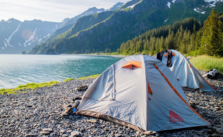 Two tents are set up on a lake shore facing mountain slopes